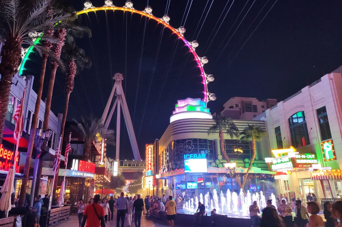 The illuminated High Roller above visitors and fountains at The LINQ Promenade at night